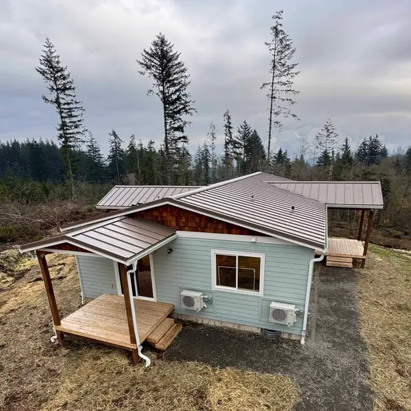 Light-blue Wolf Model I with covered wood porches and a standing-seam metal roof on a wooded hillside in Battle Ground
