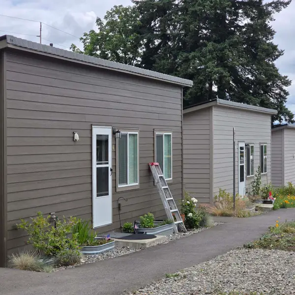 Row of finished gray and beige cottages with metal roofs along a gravel path