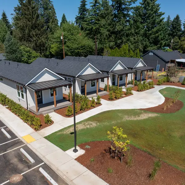 Row of finished light-gray cottages with dark roofs and covered porches along a curved walk