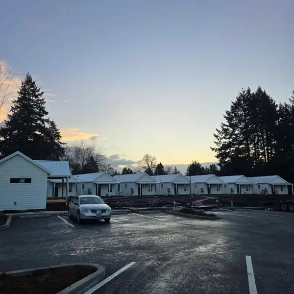 Row of finished white gable Wolf cottages beside a parking lot at dusk