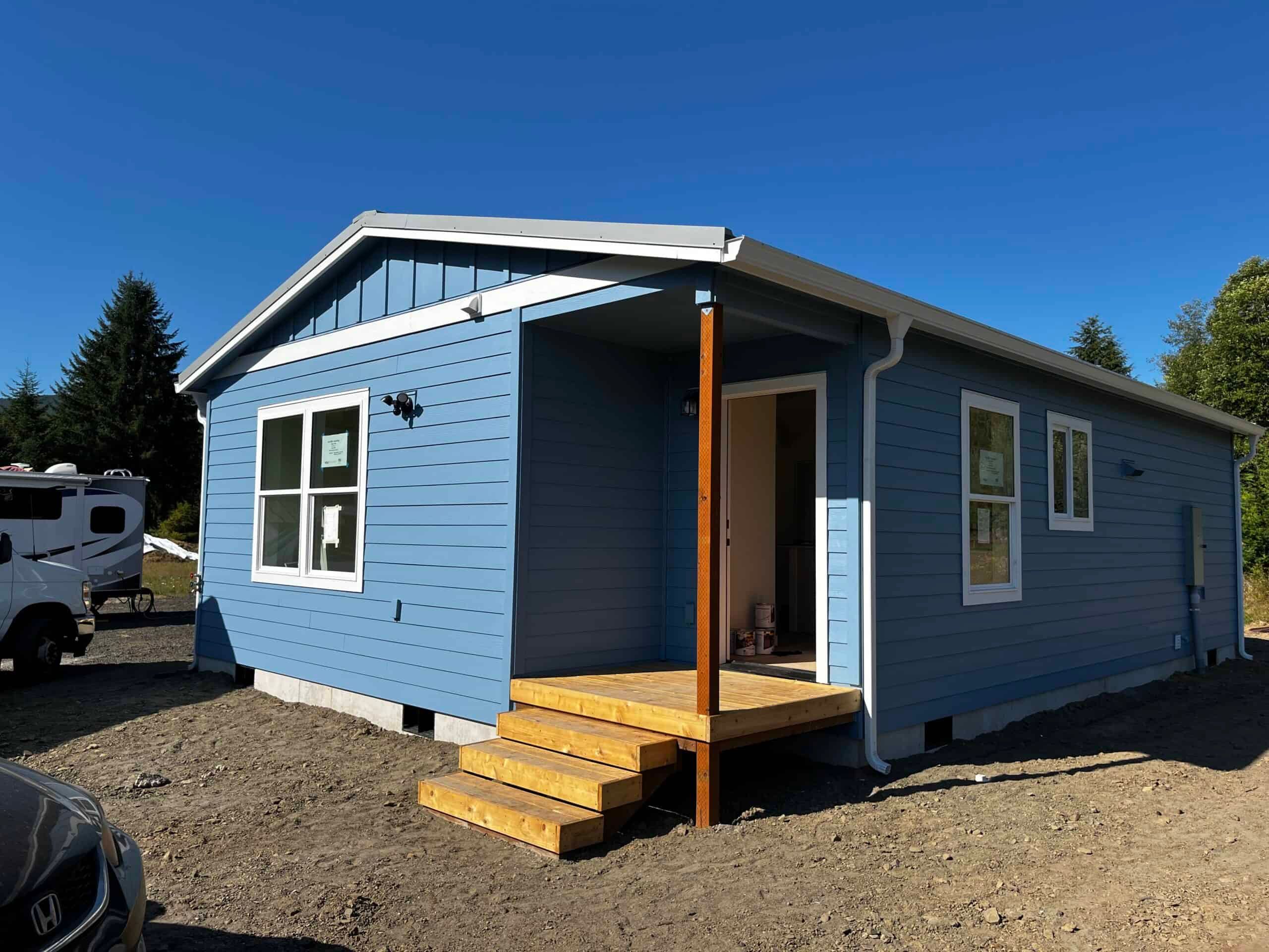 Light-blue gable Wolf Model J with a small raw-wood entry porch