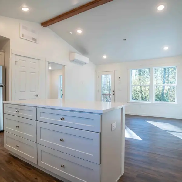 White kitchen island and stainless refrigerator opening into a living area in a Wolf Model J