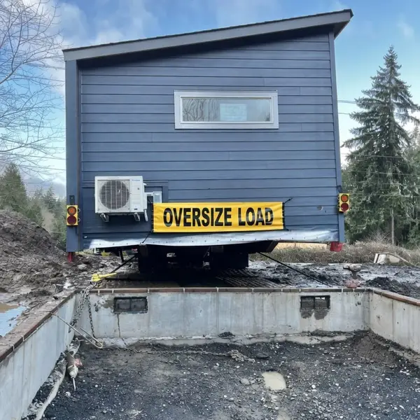 Blue-gray Wolf home on a trailer above an open foundation, marked oversize load