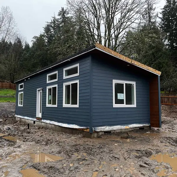 Dark blue Wolf home on a new foundation in a muddy yard, with roof sheathing still open at the gable