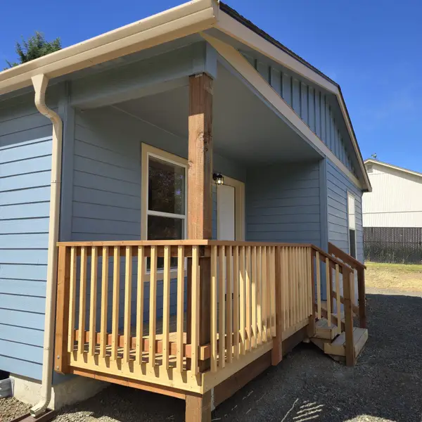 Close view of the covered wood porch, railings, and white door on a light-blue Wolf Model L