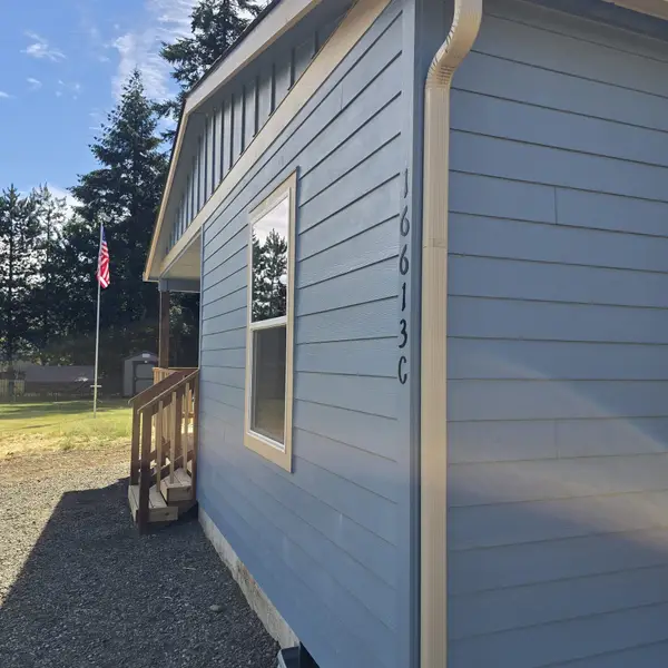 Side of a light-blue Wolf Model L with wood stairs, the address 16613 C, a flag, and evergreens