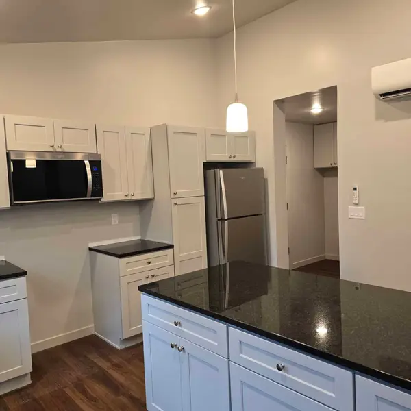 Closer view of a black stone island, white cabinets, and a stainless refrigerator in a Wolf Model L