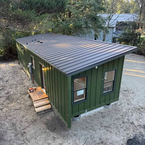 Olive-green Wolf home with a standing-seam metal roof, set on pier blocks among the trees
