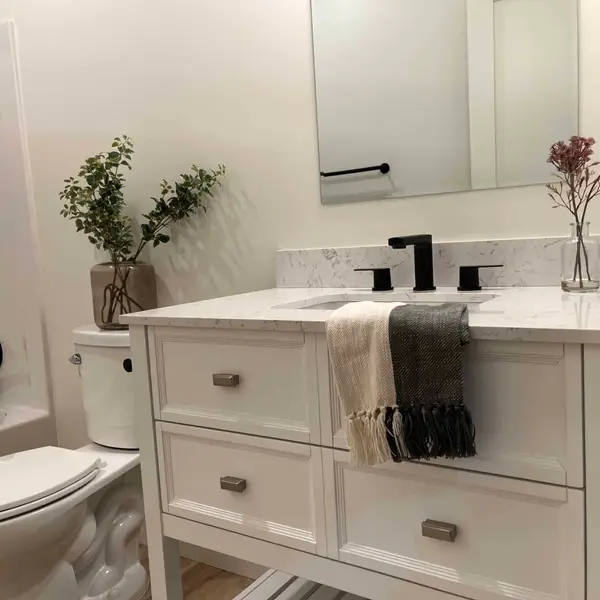 Bathroom vanity with a white top, black faucet, and a framed mirror