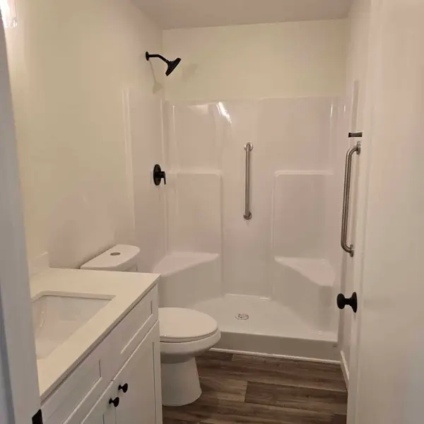 Narrow bathroom with a white one-piece shower, built-in seat, and grab bar
