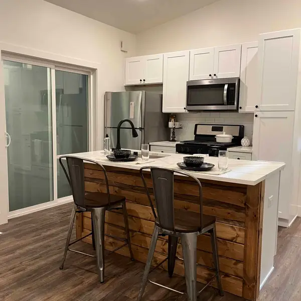 Wood-plank kitchen island with a white counter, facing white cabinets and a black range
