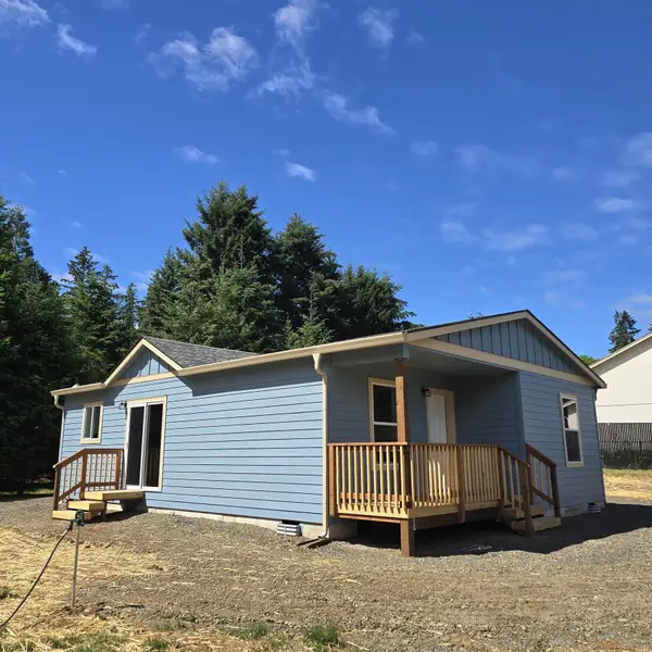 Light-blue Wolf Model L with a covered wood porch, a sliding-door deck, lap and board-and-batten siding, and evergreens behind it