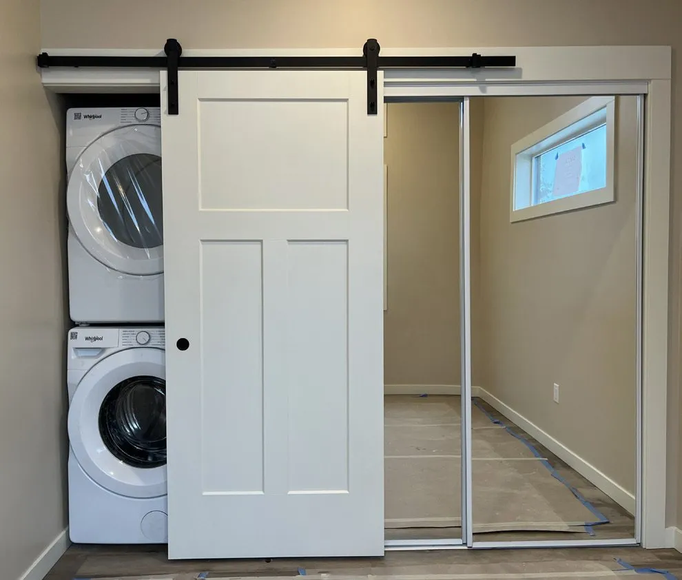 White paneled barn door on a black track in front of a stacked washer and dryer