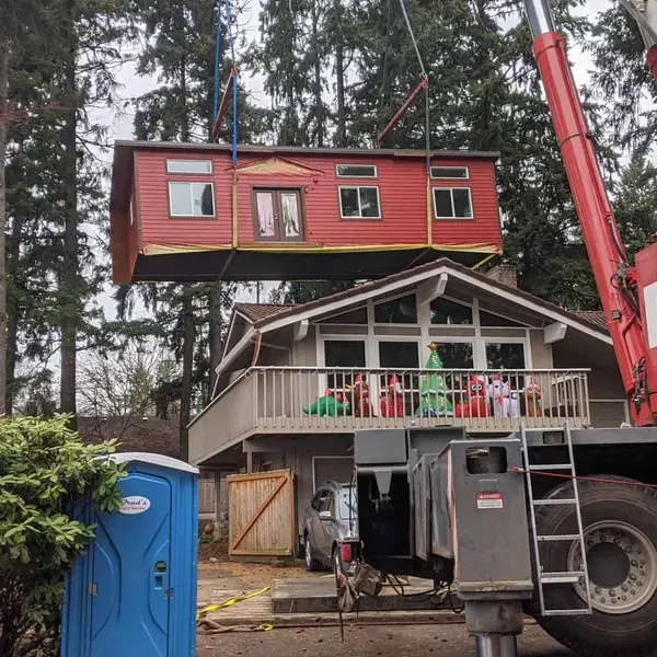 Red crane lifting a red Wolf home on straps above an existing house