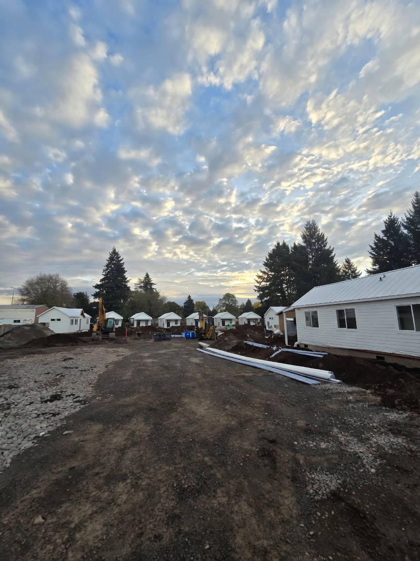 White Wolf Model F cottages set on a gravel site with excavators and utility pipes during construction.
