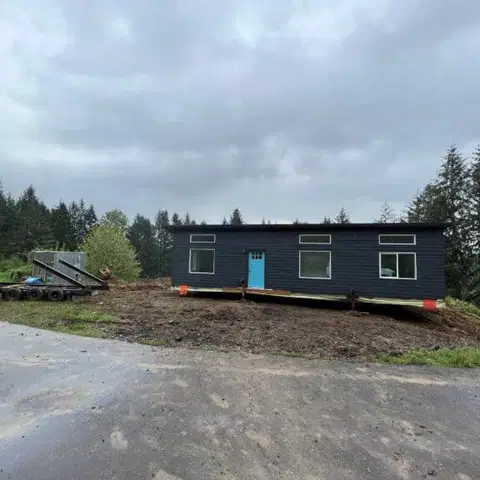 Dark navy Wolf Model E home with a blue door sitting on cribbing during delivery.