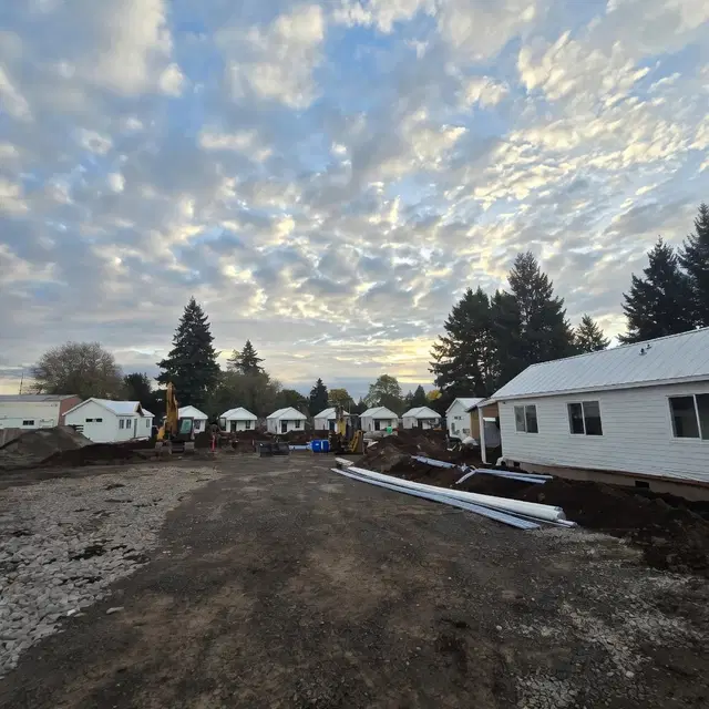 White Wolf Model F cottages set on a gravel site with excavators and utility pipes during construction.