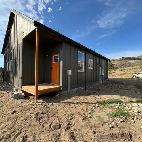 Dark gray Wolf Model J home with vertical siding, an orange door, and a small wood porch.