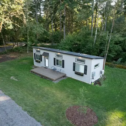 Aerial view of a light gray Wolf Model E home with black shutters and a wood deck in the trees.