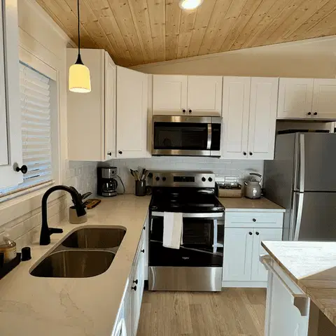 White kitchen with a wood-plank ceiling, double sink, and stainless appliances in a Wolf Model G home.