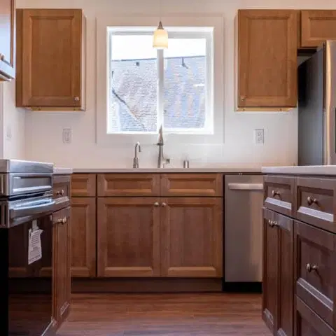 Wood kitchen with a stainless refrigerator and a window over the sink in a Wolf Model I home.