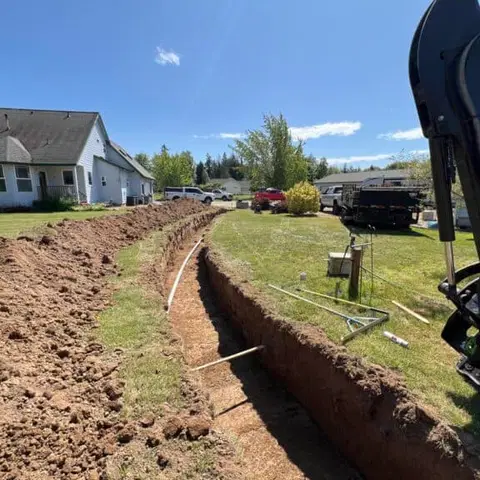 Utility trench cut across a lawn beside an excavator during site prep.