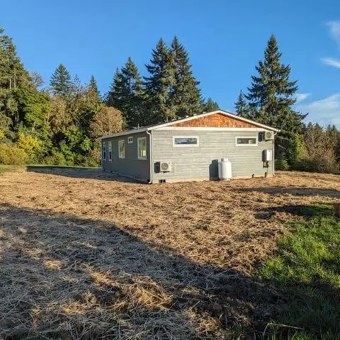 Gray Wolf Model I home with a cedar-shake gable in a field of evergreens.
