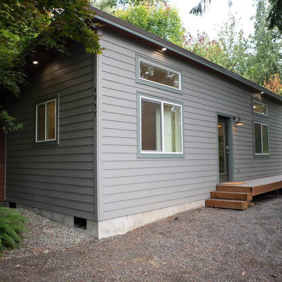 Wolf Model E home with dark grey paint and green trim with a deck that goes from the front door and wraps around the far side of the house.