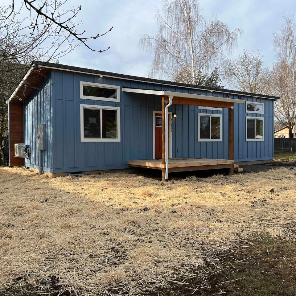 Blue and white Wolf Model E home with board and batten siding, covered porch deck, transom windows, and soffit lighting.