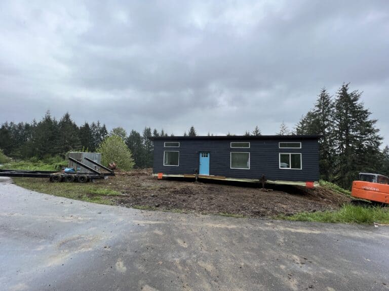 Dark navy Wolf Model E home with a blue door sitting on cribbing during delivery.