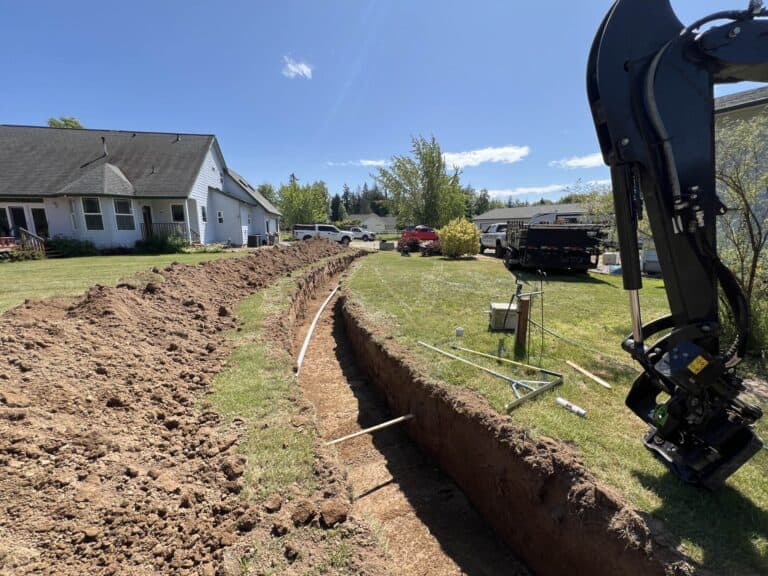Utility trench cut across a lawn beside an excavator during site prep.