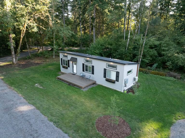 Aerial view of a light gray Wolf Model E home with black shutters and a wood deck in the trees.