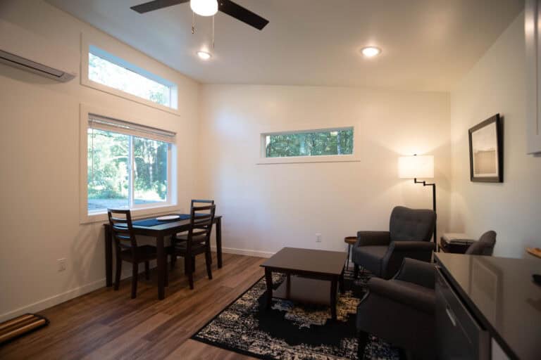 Living and dining area with transom windows and gray chairs in a Wolf Model E home.