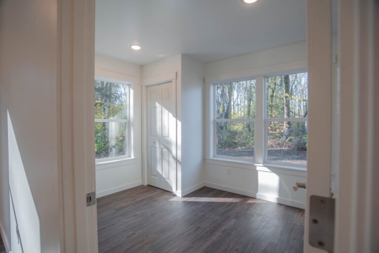 Empty room with dark flooring and windows looking into trees in a Wolf Model J home.