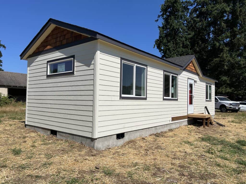 White and black Wolf Model E home with cedar shake gables and red door.